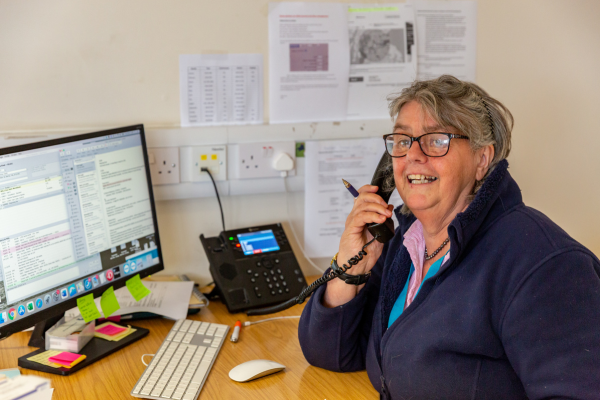 Veterinary receptionist Patty Fraser, sitting at her desk, on the phone to a client looking happy.